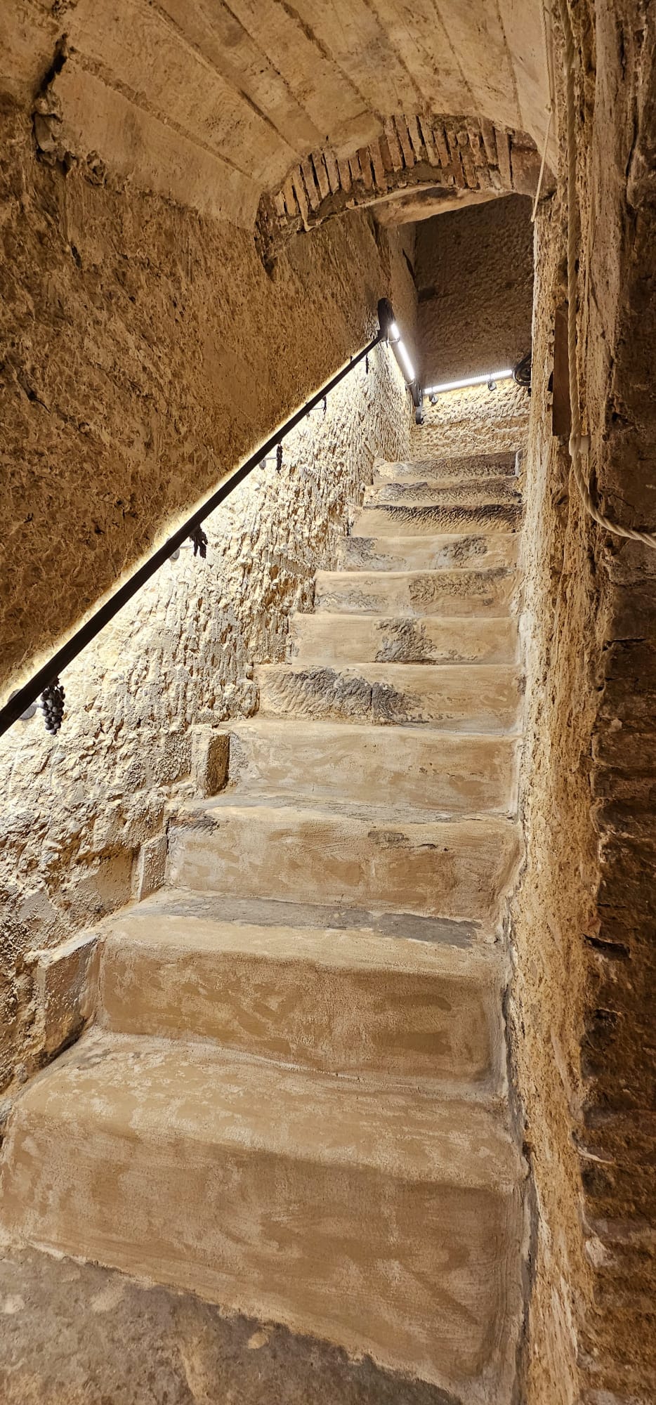 legado de ugarte alojamientos rurales escalera piedra boveda laguardia - Legado de Ugarte ofrece casas rurales y apartamentos con encanto en Laguardia, corazón de la Rioja Alavesa. Dispones de casa rural por habitaciones en la Calle Mayor y alojamientos de alquiler íntegro con jardín y barbacoa, ideales para parejas, familias y grupos que quieren disfrutar de enoturismo y del casco histórico medieval. Habitaciones y apartamentos amplios, con baño privado, WiFi y todas las comodidades para una estancia tranquila entre viñedos. Tu alojamiento rural en Laguardia para conocer bodegas, rutas del vino y los pueblos más bonitos de Rioja Alavesa. Escalera de piedra abovedada con barandilla e iluminación en alojamientos rurales.