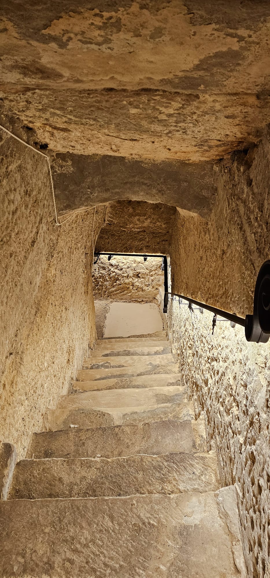 legado de ugarte alojamientos rurales escalera piedra laguardia - Legado de Ugarte ofrece casas rurales y apartamentos con encanto en Laguardia, corazón de la Rioja Alavesa. Dispones de casa rural por habitaciones en la Calle Mayor y alojamientos de alquiler íntegro con jardín y barbacoa, ideales para parejas, familias y grupos que quieren disfrutar de enoturismo y del casco histórico medieval. Habitaciones y apartamentos amplios, con baño privado, WiFi y todas las comodidades para una estancia tranquila entre viñedos. Tu alojamiento rural en Laguardia para conocer bodegas, rutas del vino y los pueblos más bonitos de Rioja Alavesa. Escalera de piedra en un pasillo subterráneo de alojamientos rurales, con barandilla y paredes de roca.